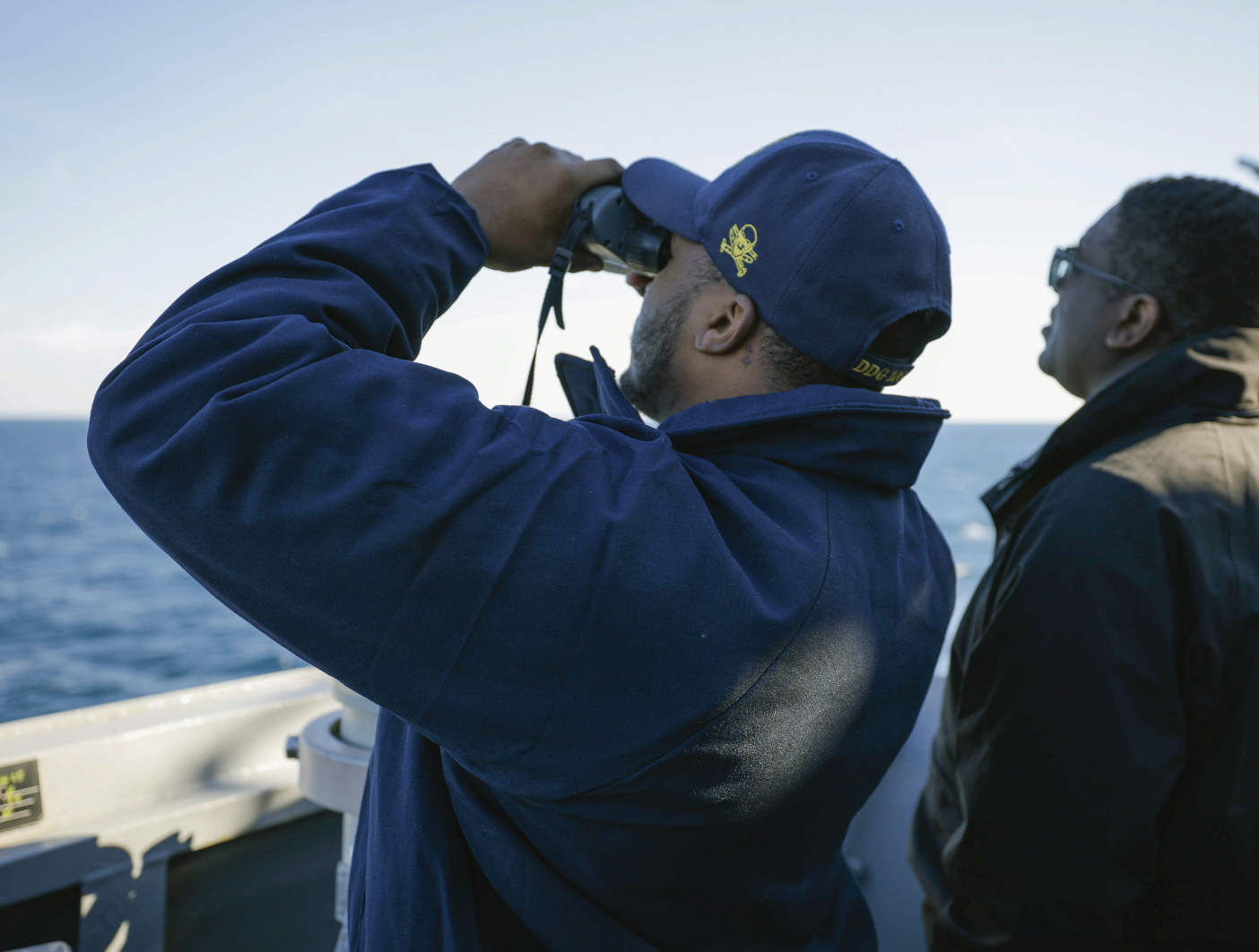 Ensign Damiyan Caldwell, left, and Commander James Koffi, right, commanding officer of guided-missile destroyer USS Truxtun, scan thehorizon for aircraft or maritime craft in proximity to ship, January 26, 2025 (U.S. Navy/Sierra Bryant)